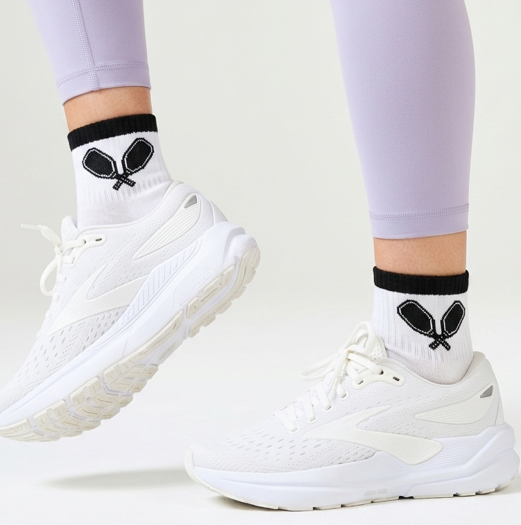 Women's white socks with black trim and black pickleball paddles.