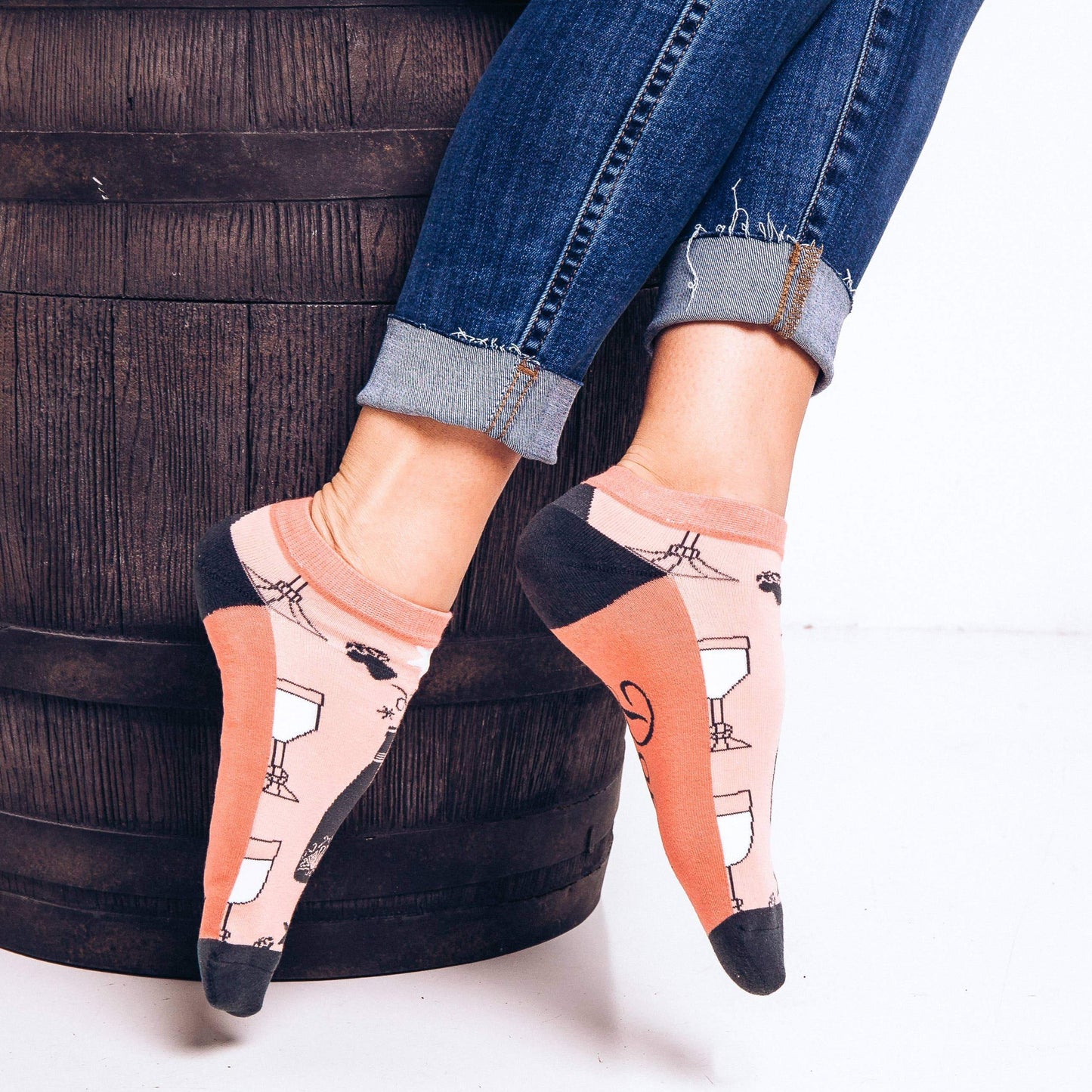 Coral-colored ankle socks with navy blue heels and toes, decorated with a pattern of wine glasses and bottles and "Wine Down" written on the soles.