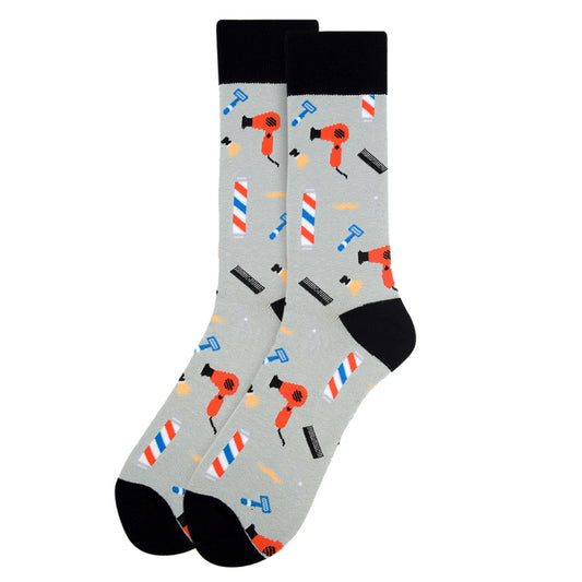 A pair of men's crew socks featuring a barber shop theme with grooming tools like hairdryers, combs, razors, and barber poles on a gray background with black accents on the toes, heels, and cuffs.