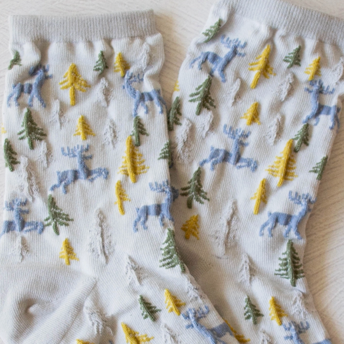Light gray cozy winter cabin socks featuring woodland deer reindeer and trees.