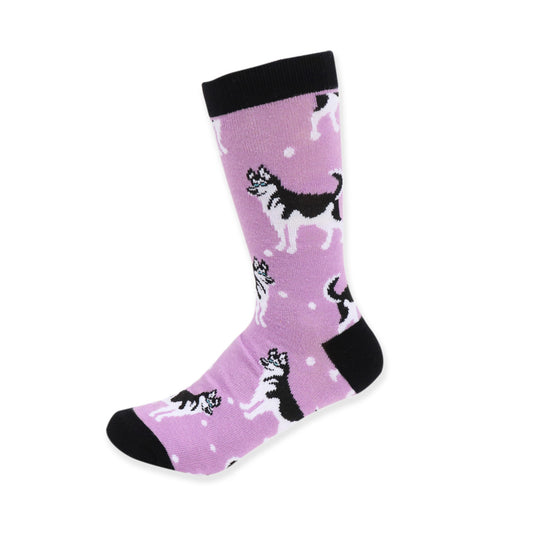 A pair of women's crew socks in a soft lilac color, patterned with black and white Siberian Husky illustrations in various poses, accented with small white dots that suggest a snowy scene. The toe, heel, and cuff of the socks are solid black, providing a contrast to the light purple background.