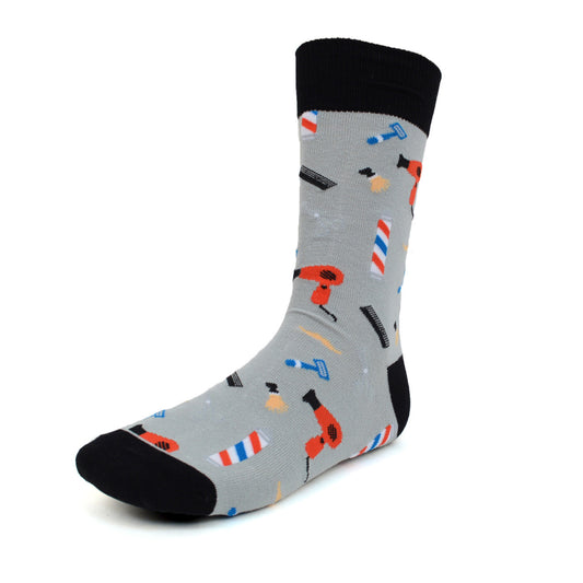 A pair of men's crew socks featuring a barber shop theme with grooming tools like hairdryers, combs, razors, and barber poles on a gray background with black accents on the toes, heels, and cuffs.