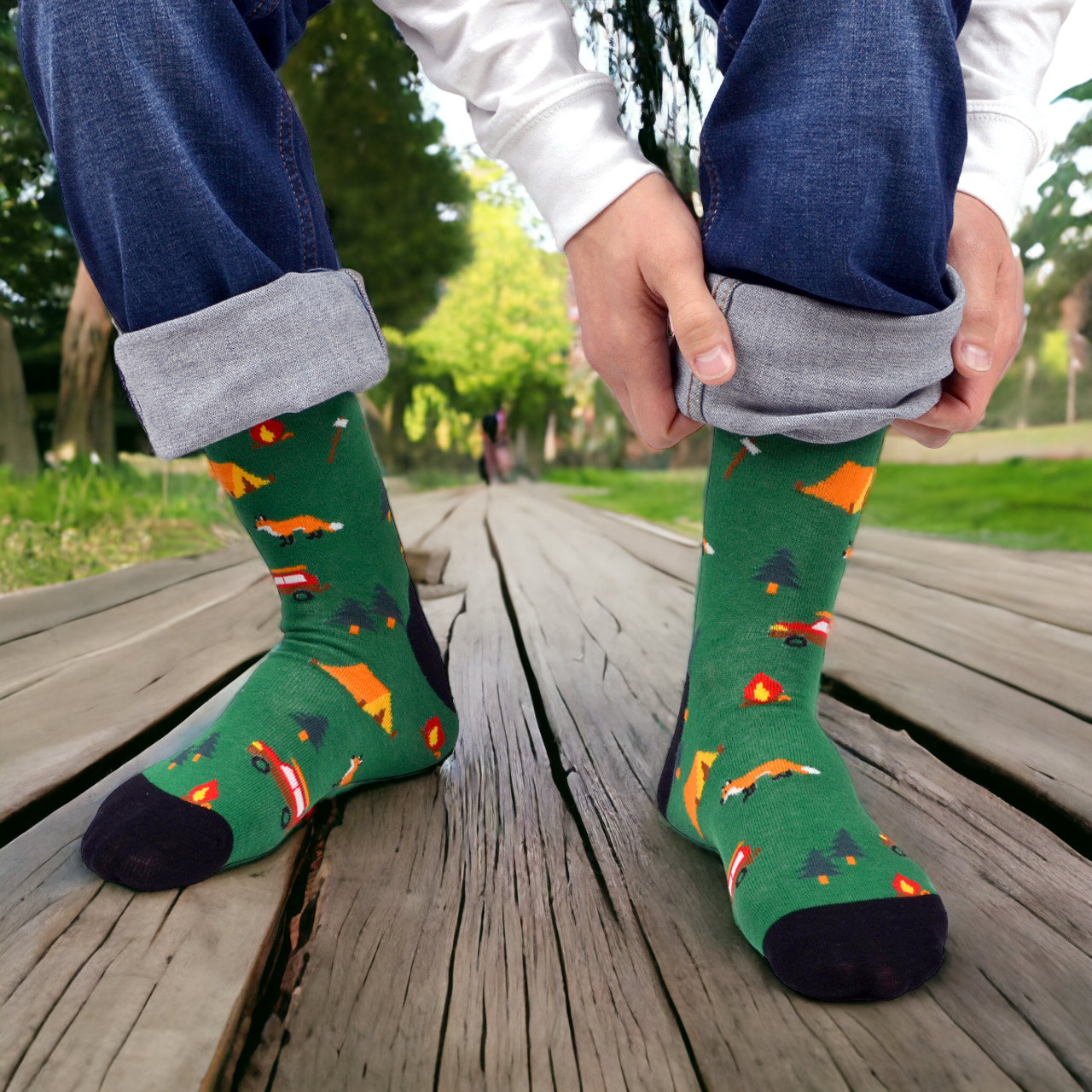 A pair of green camping crew socks with a pattern that includes tents, a fox, and a campfire.