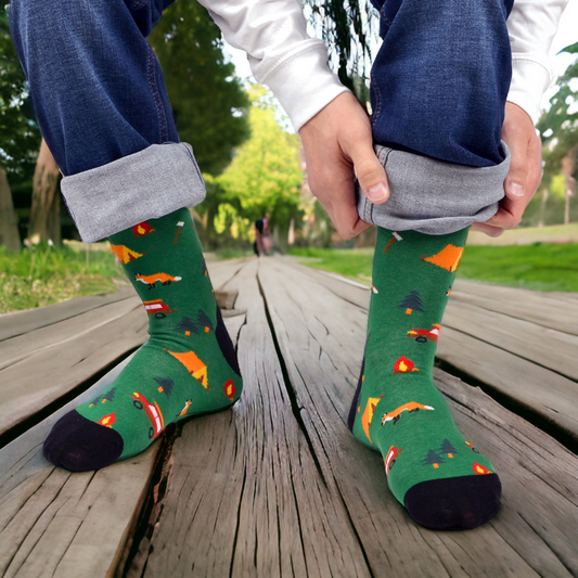 A pair of green camping crew socks with a pattern that includes tents, a fox, and a campfire.